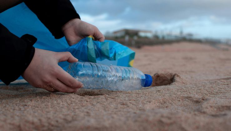 Persona che raccoglie bottiglia di plastica dalla sabbia